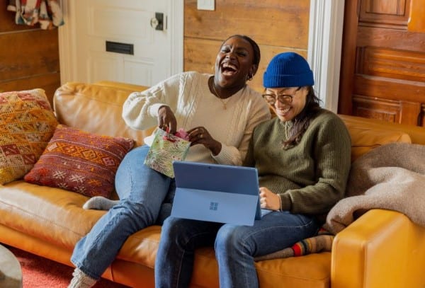 Two friends on their couch laughing while using referral bonus apps. 